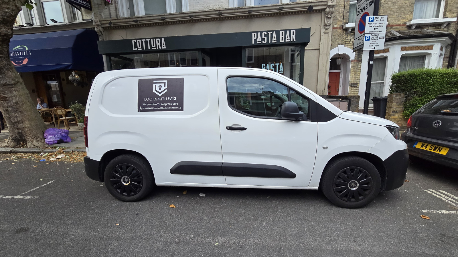 Our white van with a black background logo in front of a shop.