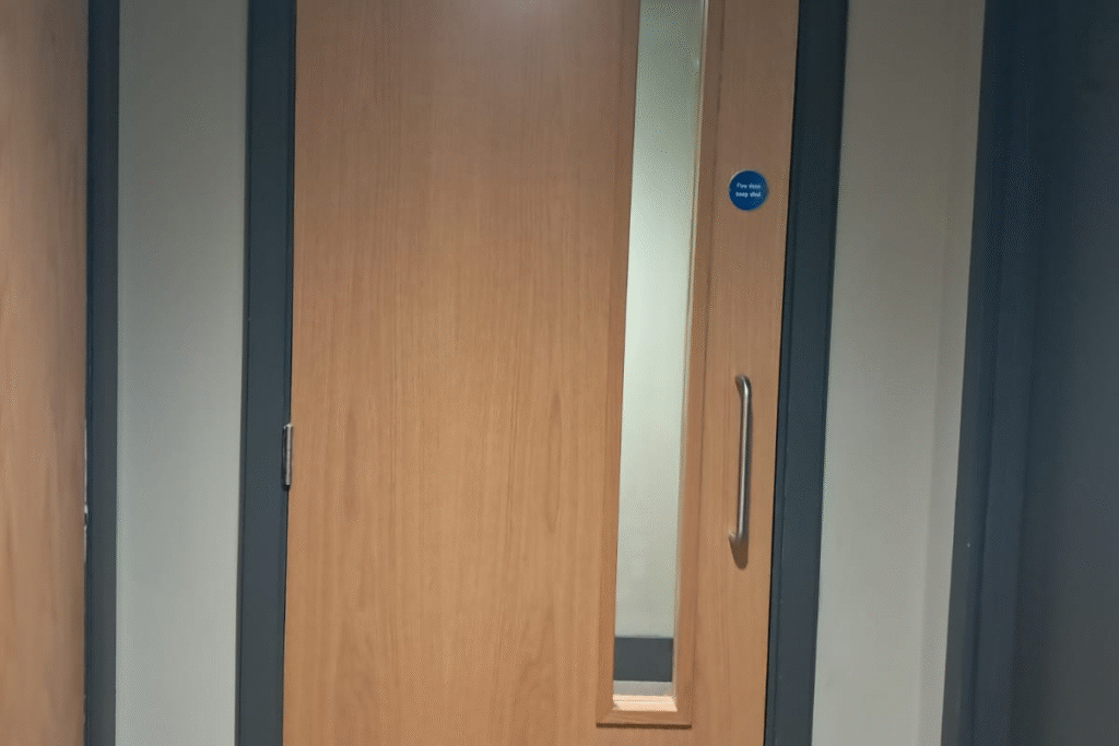 Light brown fire door with a small window and a blue rounded sign